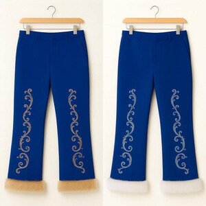 Pu&ograve; includere: Un paio di pantaloni blu reale con un ricamo verticale a volute argentate su ogni gamba e un bordo spesso in pelliccia sintetica sull'orlo. I pantaloni sono esposti su una gruccia di legno e presentano un taglio a gamba dritta.