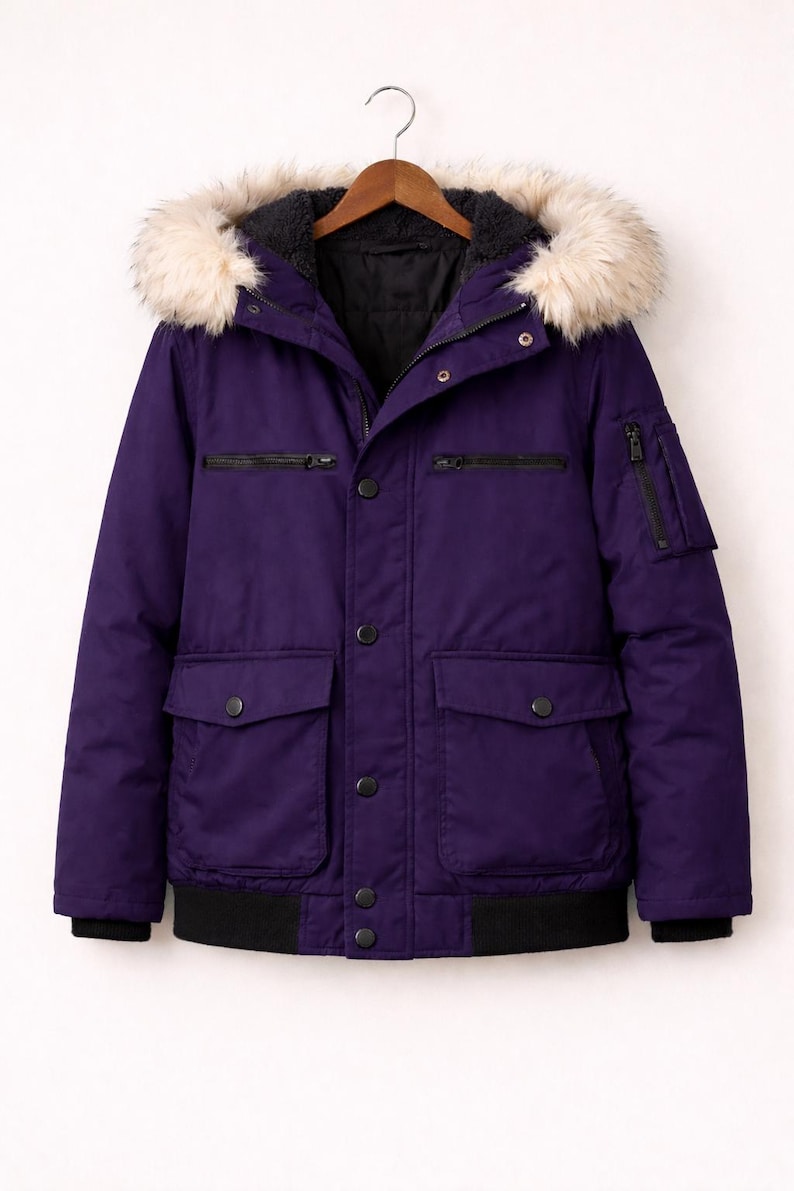 May include: A purple winter jacket with a faux fur-trimmed hood. The jacket has a black ribbed hem and cuffs, multiple pockets, and a zip and button closure. The jacket is hanging on a wooden hanger.