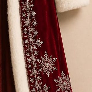 May include: A deep red velvet coat featuring a long white faux fur trim along the front opening and sleeve cuffs. The front panel is decorated with intricate silver embroidered snowflake patterns of varying sizes arranged vertically.