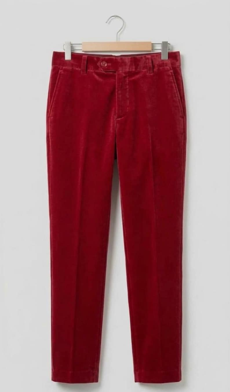 May include: Deep red velvet trousers featuring a structured waistband with a single button closure, belt loops, and a front zipper fly. The pants have a straight-leg cut with a visible pressed crease running down the center of each leg.