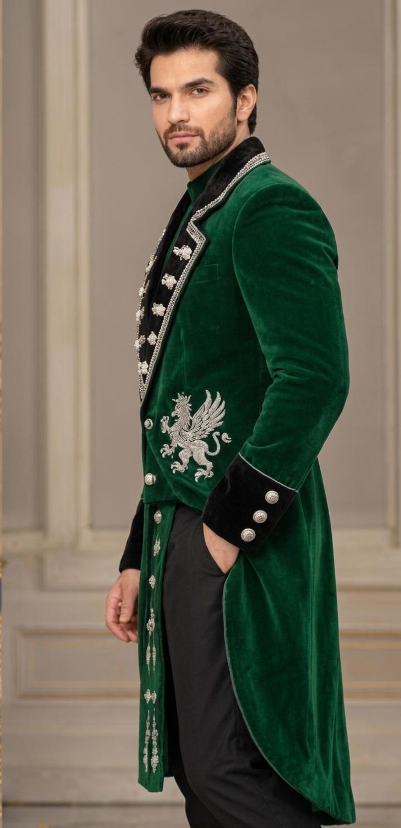 May include: A long-length emerald green velvet coat featuring a black velvet lapel, silver metallic embroidery of a griffin on the side, and silver buttons along the front closure and cuffs, paired with plain black trousers.