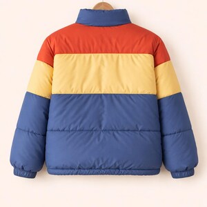 May include: A color-blocked puffer jacket in red, yellow, and blue. The jacket has a high collar and elastic cuffs. The jacket is hanging on a wooden hanger. The jacket is a casual outerwear garment.