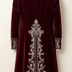Pu&ograve; includere: Un cappotto lungo in velluto bordeaux caratterizzato da intricati ricami argentati sul pannello posteriore, sul colletto e sui polsini delle maniche. Il cappotto ha una vestibilit&agrave; strutturata con uno spacco centrale posteriore ed &egrave; appeso a una gruccia in legno.