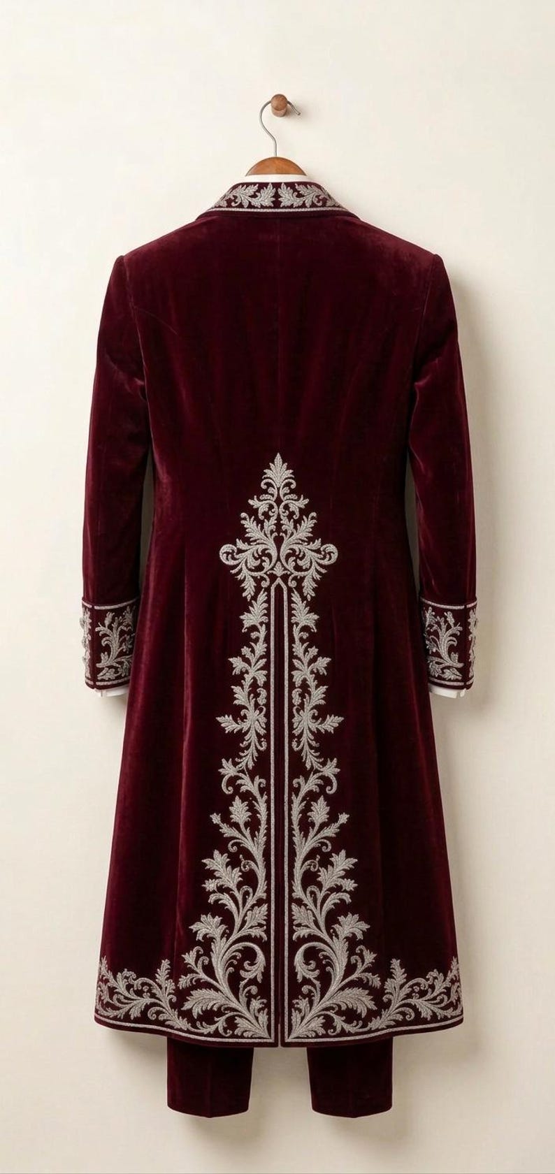 Pu&ograve; includere: Un cappotto lungo in velluto bordeaux caratterizzato da intricati ricami argentati sul pannello posteriore, sul colletto e sui polsini delle maniche. Il cappotto ha una vestibilit&agrave; strutturata con uno spacco centrale posteriore ed &egrave; appeso a una gruccia in legno.