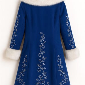 May include: A royal blue coat featuring a white faux fur collar, cuffs, and hem. The coat is decorated with silver-toned swirling floral embroidery patterns running vertically down the center back and along the length of each sleeve.