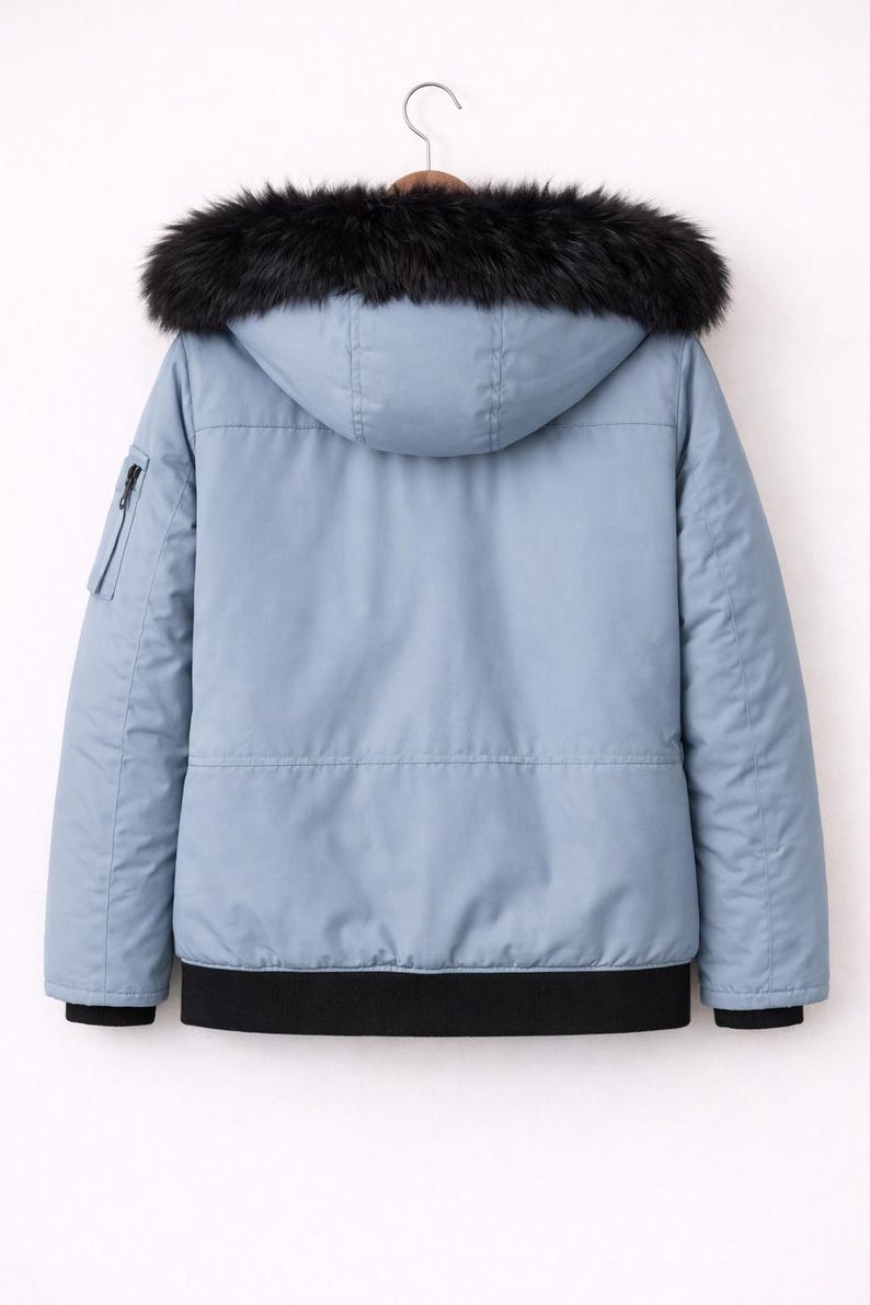 Pode incluir: Casaco de inverno azul claro com capuz forrado a p&ecirc;lo sint&eacute;tico preto. O casaco tem um bolso com z&iacute;per na manga esquerda e uma bainha canelada preta. O casaco est&aacute; pendurado num cabide de madeira.