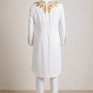 May include: A white long-length coat and matching trousers. The coat features gold embroidery across the upper back and shoulders, with additional gold embroidery on the sleeve cuffs. The garment is displayed on a mannequin from the rear view.