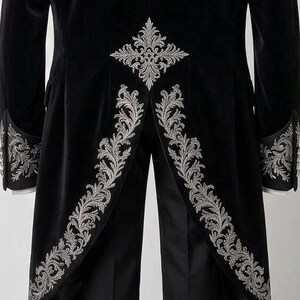 May include: A black velvet tailcoat featuring intricate silver embroidery along the cuffs and the back panels. The design includes a prominent floral-inspired motif centered at the waist and scrolling leaf patterns lining the coat tails.