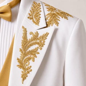 May include: A white blazer featuring intricate gold leaf embroidery on the lapel and shoulder. The garment is paired with a white pleated shirt and a solid gold bow tie, creating a formal ensemble with detailed metallic stitching throughout.