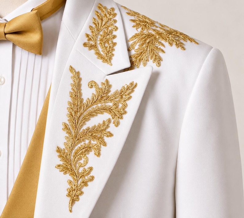 May include: A white blazer featuring intricate gold leaf embroidery on the lapel and shoulder. The garment is paired with a white pleated shirt and a solid gold bow tie, creating a formal ensemble with detailed metallic stitching throughout.