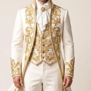 May include: A white tailcoat suit featuring intricate gold embroidery along the lapels, cuffs, and vest. The ensemble includes a white shirt with a high collar, a white cravat secured with a gold brooch, and matching white trousers.