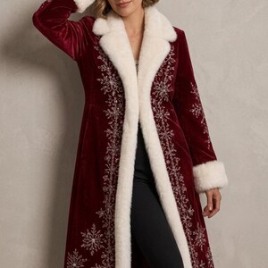 May include: A long, deep red velvet coat featuring white faux fur trim on the collar, cuffs, and hem. The coat is decorated with intricate silver embroidered snowflake patterns along the front panels and lower sections of the garment.