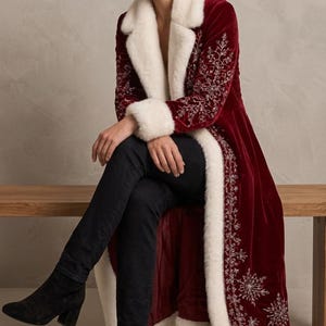 May include: A long, deep red velvet coat featuring white faux fur trim along the collar, cuffs, and front opening. The coat is decorated with intricate silver embroidered snowflake and vine patterns along the sleeves and front panels.