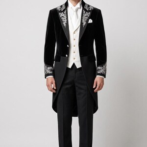May include: A black velvet tailcoat featuring silver floral embroidery on the lapels and cuffs, paired with a white vest with gold buttons, a white dress shirt, a white necktie, black trousers, and black dress shoes.