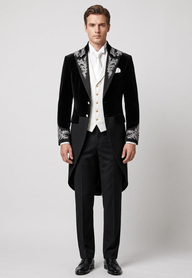 May include: A black velvet tailcoat featuring silver floral embroidery on the lapels and cuffs, paired with a white vest with gold buttons, a white dress shirt, a white necktie, black trousers, and black dress shoes.