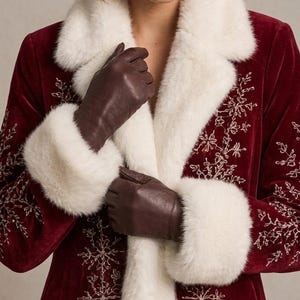 May include: A deep red velvet coat featuring a white faux fur collar and cuffs, adorned with intricate silver embroidered snowflake patterns along the front panels, paired with dark brown leather gloves that reach the wrists.