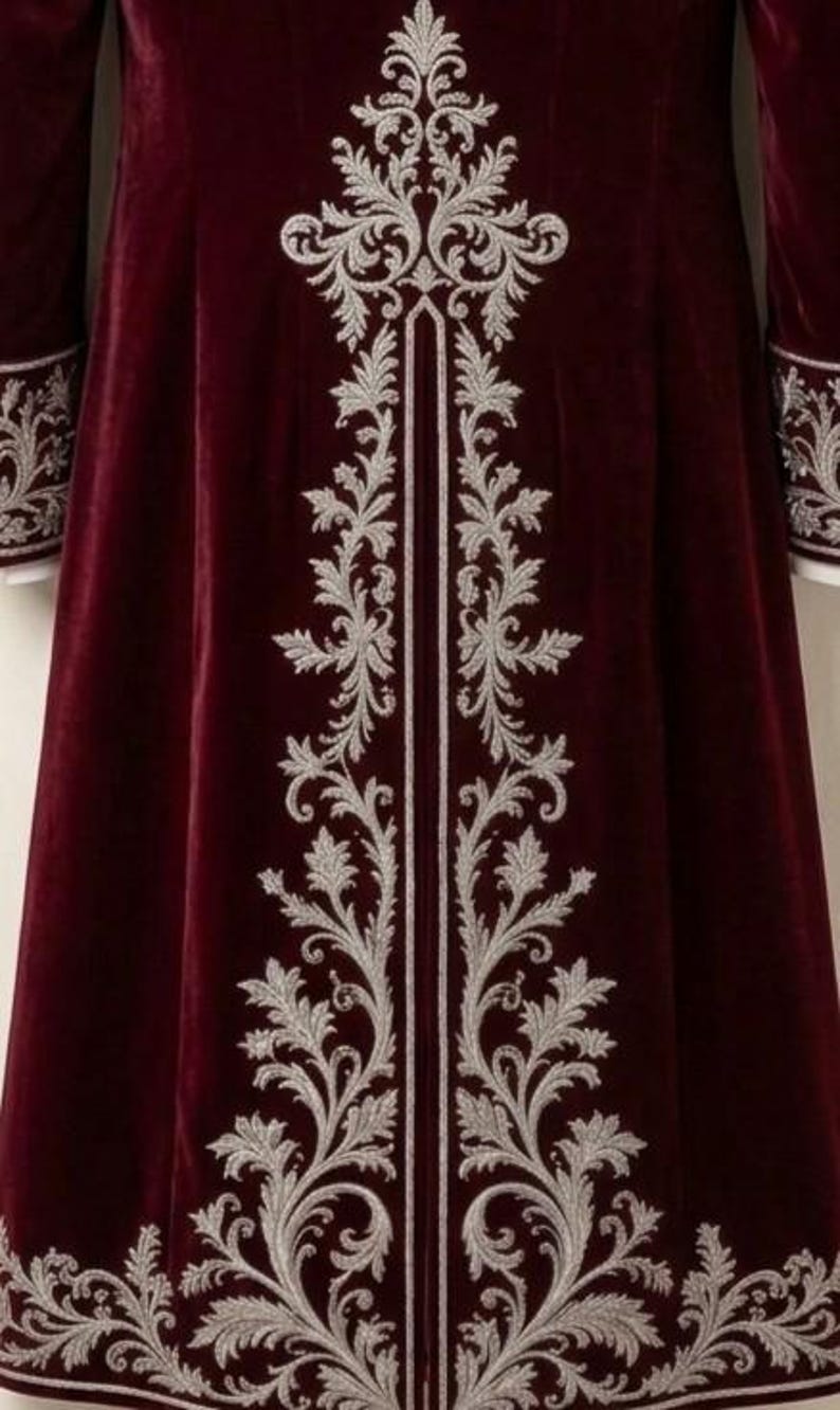 Pu&ograve; includere: Un cappotto in velluto bordeaux intenso caratterizzato da un intricato ricamo argentato che corre verticalmente lungo il centro e l'orlo. Le maniche lunghe sono rifinite con polsini ricamati in argento abbinati, creando un design dettagliato.