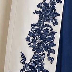 May include: A white garment panel featuring an intricate dark blue floral embroidery pattern running vertically along the edge. The embroidery consists of detailed leaves and blossoms, contrasting sharply against the smooth white fabric base.