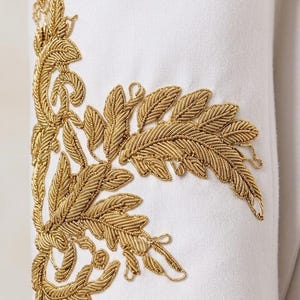 May include: A white garment sleeve featuring intricate gold metallic thread embroidery in a detailed fern leaf pattern. The embroidery is applied vertically along the side of the sleeve, showcasing textured stitching and organic botanical shapes.