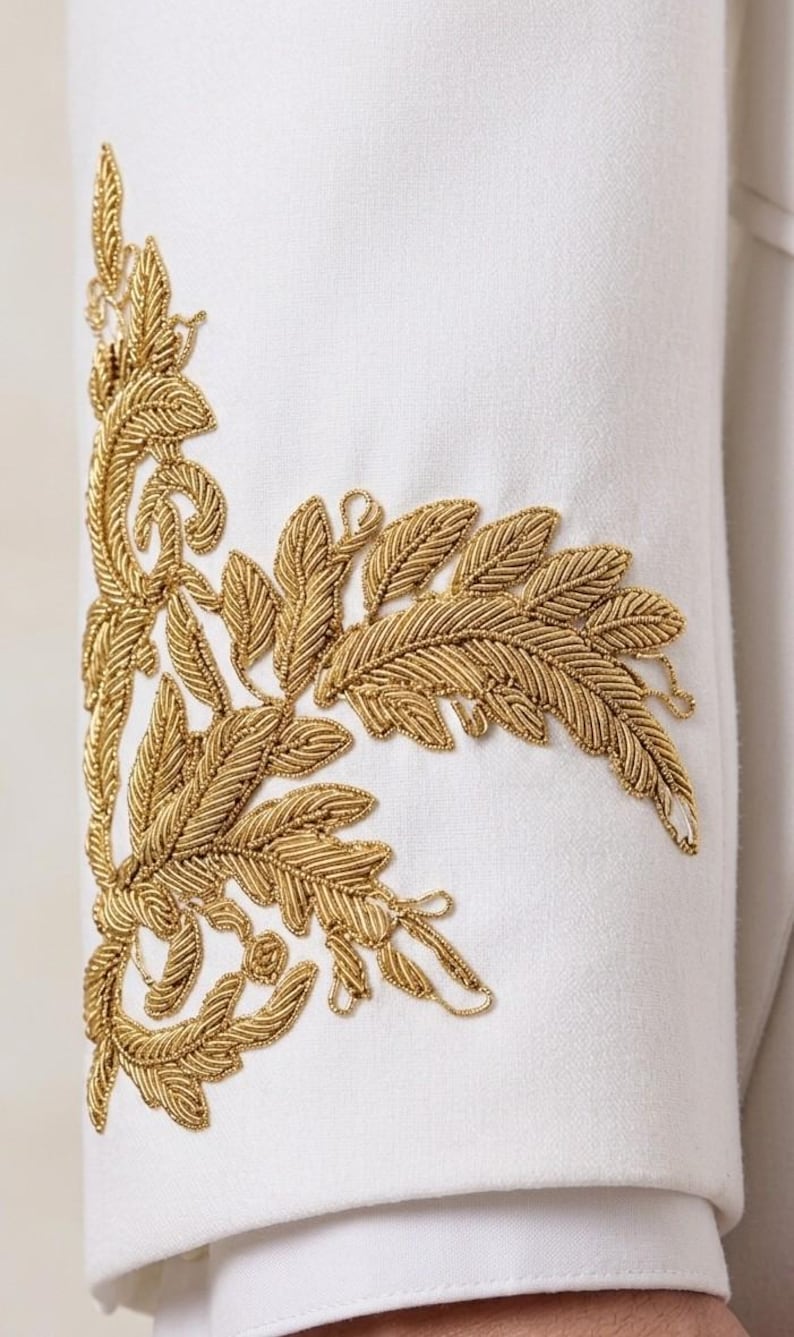 May include: A white garment sleeve featuring intricate gold metallic thread embroidery in a detailed fern leaf pattern. The embroidery is applied vertically along the side of the sleeve, showcasing textured stitching and organic botanical shapes.