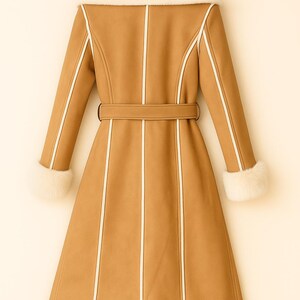 May include: A tan coat with a faux fur collar and cuffs, and a matching belt. The coat has white trim along the seams and down the front. The coat is hanging on a wooden hanger.