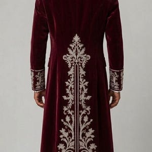 Pu&ograve; includere: Un cappotto lungo in velluto bordeaux intenso con intricati ricami color argento sul retro, sui polsini e sul colletto. Il cappotto presenta una vestibilit&agrave; strutturata, maniche lunghe e un motivo floreale verticale centrale sulla schiena.
