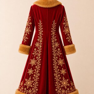 May include: A long, deep red velvet coat featuring a tan faux fur collar and cuffs. The coat is decorated with intricate gold embroidery in snowflake and vine patterns along the sleeves and the full-length skirt, hanging on a wooden hanger.