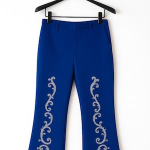 Pu&ograve; includere: Pantaloni blu reale con gamba a zampa e vita con passanti per cintura. La parte anteriore di ogni gamba &egrave; decorata con un motivo verticale e simmetrico a volute color argento, ricamato lungo il centro del tessuto.