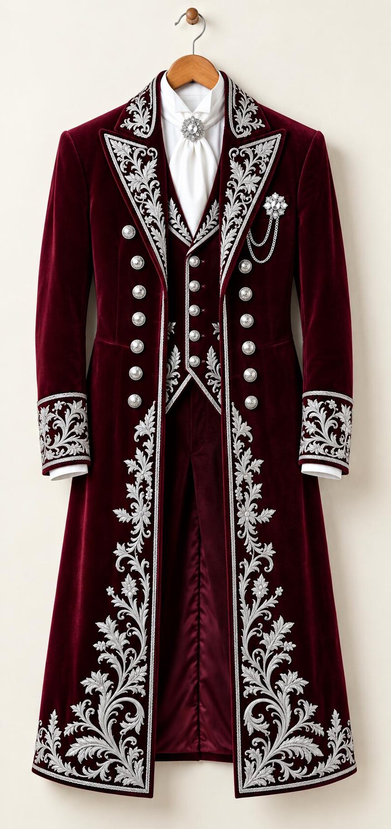 Pu&ograve; includere: Un frac in velluto bordeaux intenso e gilet abbinato con intricati ricami floreali argentati su revers, polsini e orlo. Il set include bottoni argentati, una cravatta bianca con spilla di cristallo e un accessorio a catena argentata.