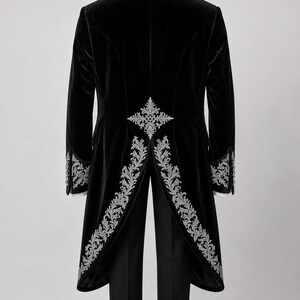 May include: A black velvet tailcoat featuring intricate silver embroidery along the back vent, waist, and sleeve cuffs. The coat is paired with matching black trousers and black dress shoes, displayed on a hanger against a neutral background.