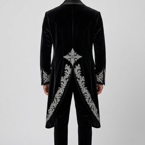 May include: A black velvet tailcoat and matching trousers featuring intricate silver embroidery along the back vent, hem, and cuffs. The tailcoat has a structured silhouette with a high collar and long tails, paired with slim-fit black velvet trousers.