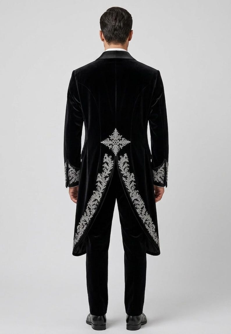 May include: A black velvet tailcoat and matching trousers featuring intricate silver embroidery along the back vent, hem, and cuffs. The tailcoat has a structured silhouette with a high collar and long tails, paired with slim-fit black velvet trousers.