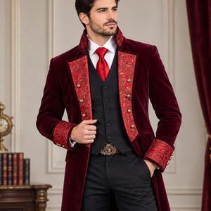 Puede incluir: Un abrigo largo de terciopelo color burdeos profundo con solapas y pu&ntilde;os de brocado rojo y dorado adornados con botones dorados, sobre un chaleco negro, una camisa blanca de cuello, una corbata roja brillante y pantalones negros con hebilla dorada.