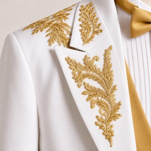 May include: A white blazer featuring intricate gold metallic embroidery in a fern-like leaf pattern on the lapel and shoulder. The garment is paired with a white pleated shirt and a solid gold satin bow tie, creating a formal ensemble.