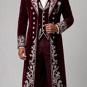 Pu&ograve; includere: Un cappotto lungo in velluto bordeaux intenso e un gilet abbinato con intricati ricami floreali argentati, bottoni argentati e una cravatta bianca. L'insieme include pantaloni bordeaux scuro e scarpe eleganti in pelle nera.