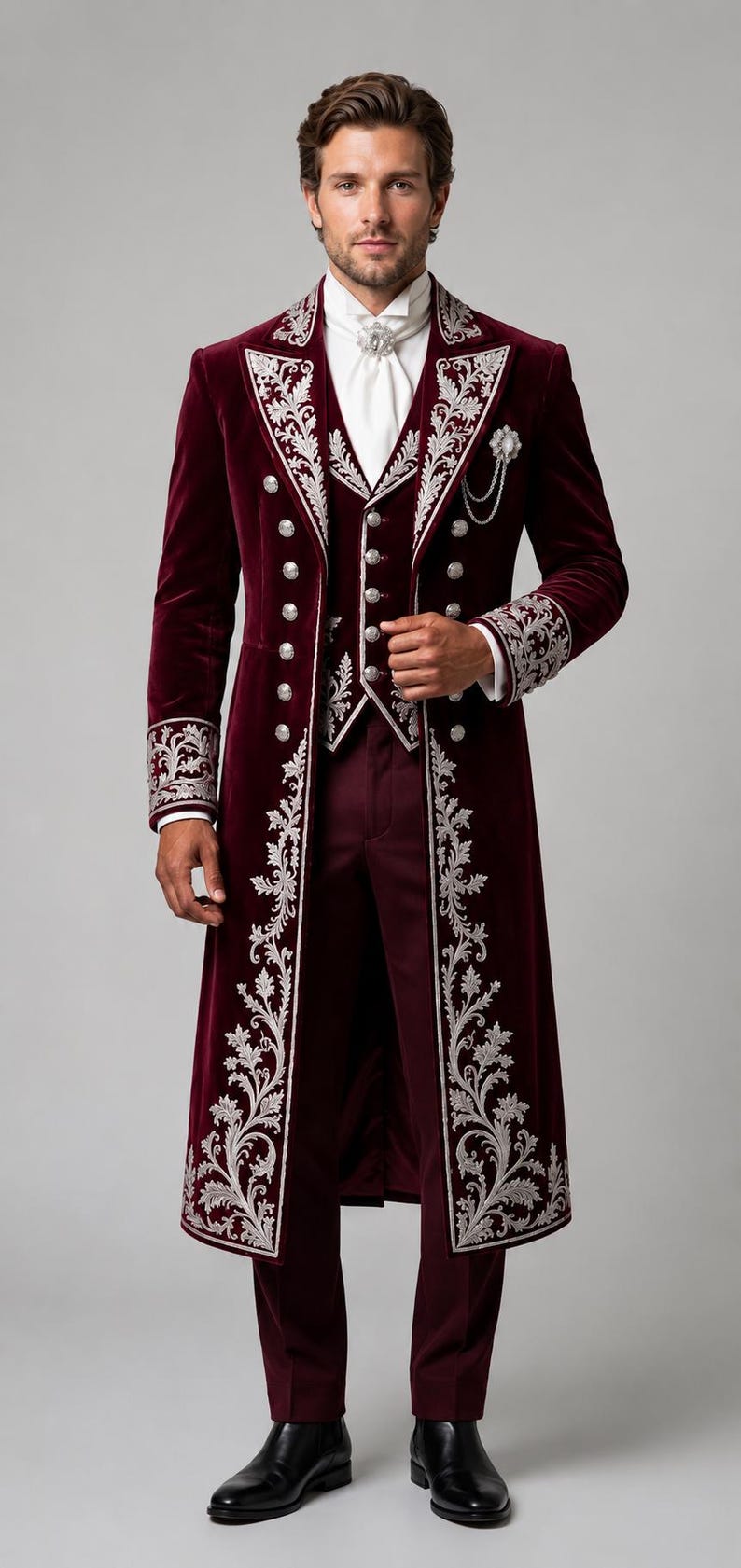 Pu&ograve; includere: Un cappotto lungo in velluto bordeaux intenso e un gilet abbinato con intricati ricami floreali argentati, bottoni argentati e una cravatta bianca. L'insieme include pantaloni bordeaux scuro e scarpe eleganti in pelle nera.