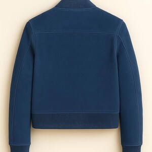 May include: A navy blue bomber jacket with a ribbed collar, cuffs, and hem, hanging on a wooden hanger. The back of the jacket is visible, showing its tailored design. The jacket's colour is a deep, rich blue.