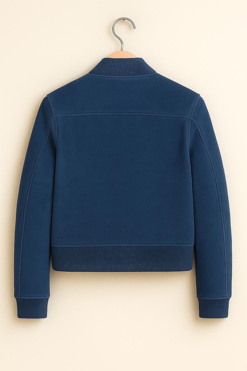 May include: A navy blue bomber jacket with a ribbed collar, cuffs, and hem, hanging on a wooden hanger. The back of the jacket is visible, showing its tailored design. The jacket's colour is a deep, rich blue.