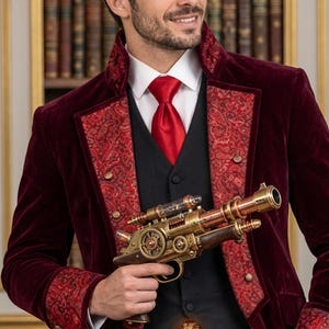 Puede incluir: Un abrigo de terciopelo color burdeos profundo con solapas y pu&ntilde;os de cachemira roja, sobre un chaleco negro, camisa blanca y corbata roja. Una pistola de utiler&iacute;a estilo steampunk de metal dorado con engranajes y un tubo de vidrio.