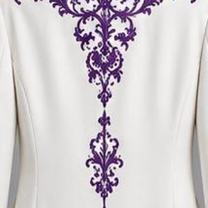 May include: A white blazer featuring a prominent, intricate purple embroidery design centered on the back. The embroidery displays a detailed, symmetrical scrollwork pattern that extends vertically from the shoulder area down the center back.
