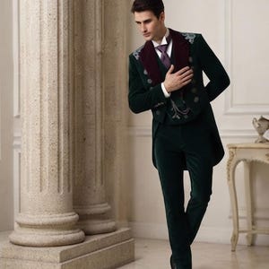 May include: A dark green velvet tailcoat suit featuring a deep burgundy velvet lapel, silver-toned buttons, and intricate silver embroidery on the shoulders. The ensemble includes a white collared shirt, a purple necktie, and a matching velvet vest.