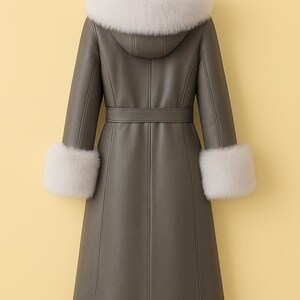 May include: A long, olive-green coat with a hood and a belt. The hood and cuffs are trimmed with white fur. The coat is hanging on a hook against a yellow background.