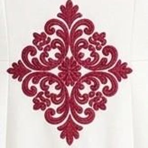 May include: A white fabric surface featuring a large, symmetrical, diamond-shaped embroidery pattern in deep red thread. The design consists of intricate, swirling scrollwork and floral-inspired motifs centered in a vertical orientation.