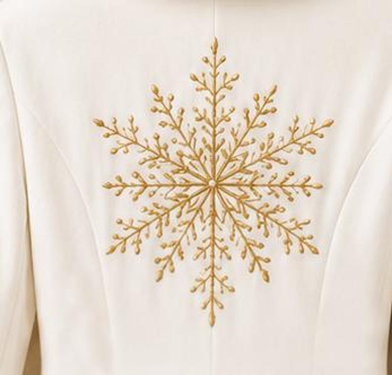 May include: A white garment featuring a large, centered, gold-colored embroidered snowflake design. The embroidery consists of intricate, branching lines radiating from a central point, creating a detailed, symmetrical, and metallic-toned pattern.