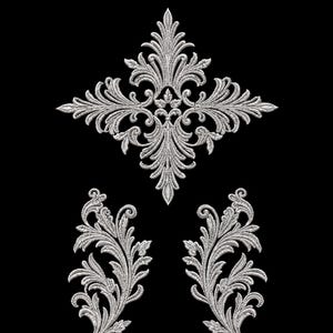 May include: A set of three silver-colored embroidered appliques featuring intricate acanthus leaf and scrollwork patterns. One large diamond-shaped central piece is positioned above two smaller, symmetrical, upward-curving leaf motifs.