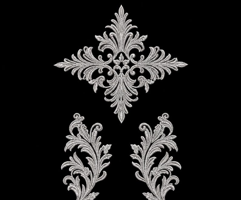 May include: A set of three silver-colored embroidered appliques featuring intricate acanthus leaf and scrollwork patterns. One large diamond-shaped central piece is positioned above two smaller, symmetrical, upward-curving leaf motifs.