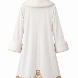 May include: A long white coat featuring a plush faux fur collar and matching cuffs on the sleeves. The hem of the coat is decorated with an intricate gold embroidered scrollwork pattern. The garment is displayed on a wooden hanger against a white background.