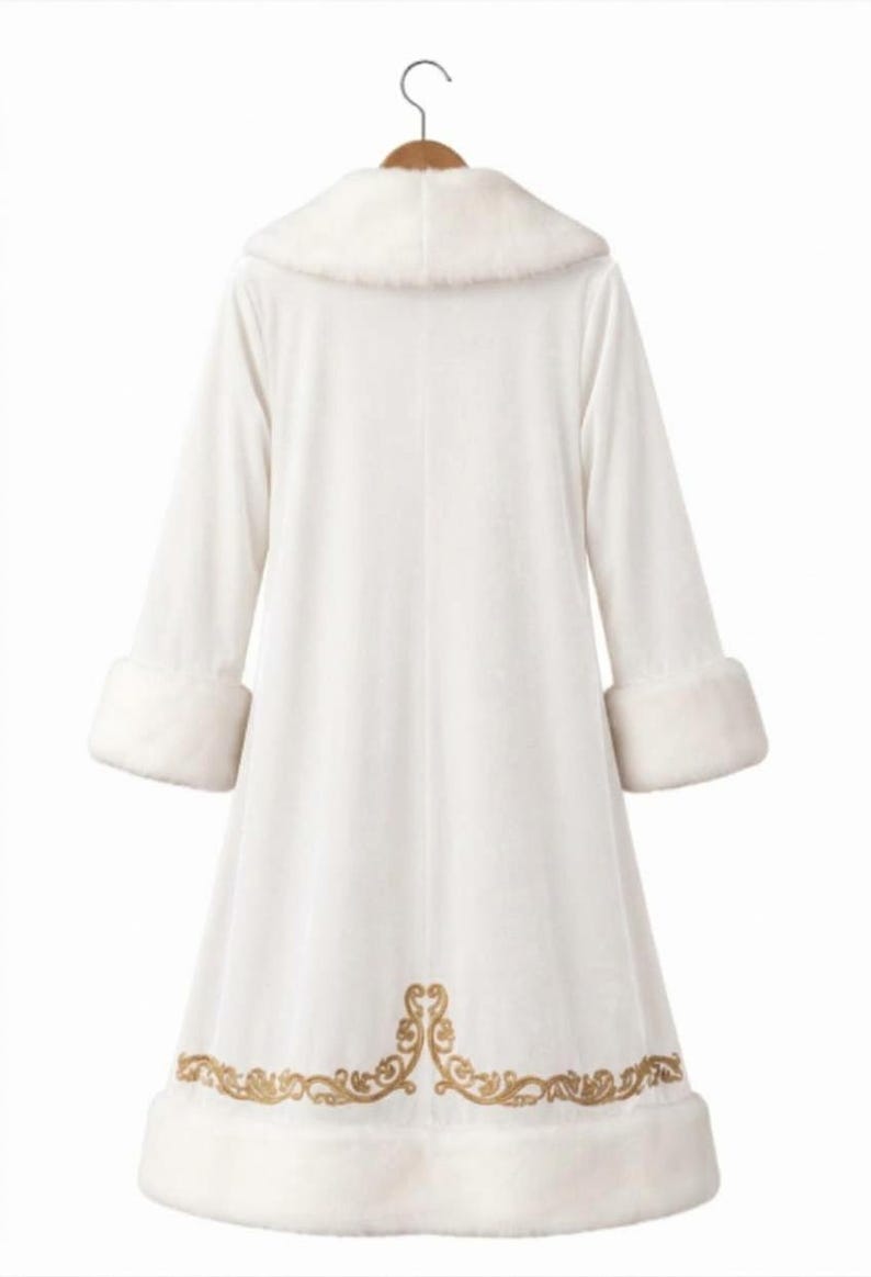 May include: A long white coat featuring a plush faux fur collar and matching cuffs on the sleeves. The hem of the coat is decorated with an intricate gold embroidered scrollwork pattern. The garment is displayed on a wooden hanger against a white background.