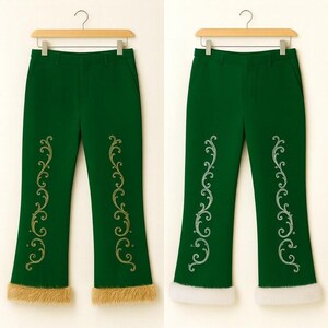 Puede incluir: Dos pantalones de color verde oscuro colgados en perchas de madera. Cada par presenta un bordado de volutas doradas en la parte delantera de las piernas y un borde grueso de piel sint&eacute;tica en el bajo de los pantalones.