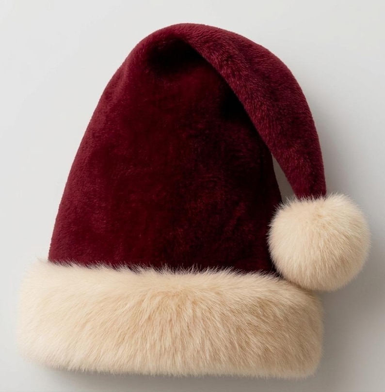 Pu&ograve; includere: Un cappello da Babbo Natale color bordeaux intenso realizzato in materiale morbido e felpato. Il cappello presenta un'ampia bordatura in pelliccia sintetica color crema alla base e un pon-pon coordinato fissato sulla punta ripiegata.